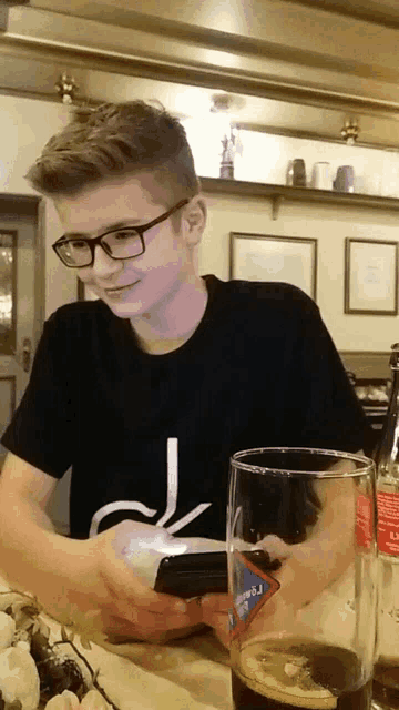 a young man sitting at a table with a glass of soda and a cell phone