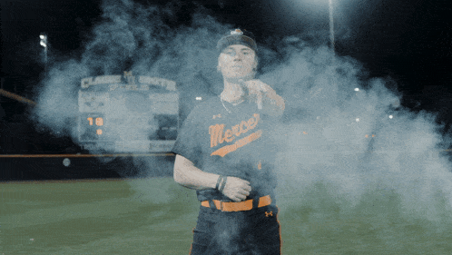 a baseball player wearing a mercer jersey stands in smoke