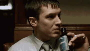 a man in a tie is drinking a beer from a bottle .