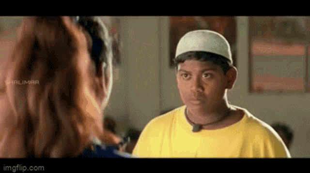 a man in a yellow shirt and a white hat is talking to a woman in a room .