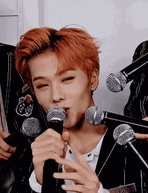 a young man with red hair is singing into a microphone while holding another microphone .