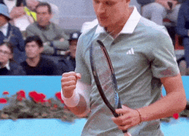a man in an adidas shirt holds a tennis racket