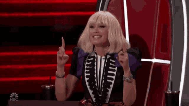 a woman in a skeleton outfit is sitting in a chair and pointing up .