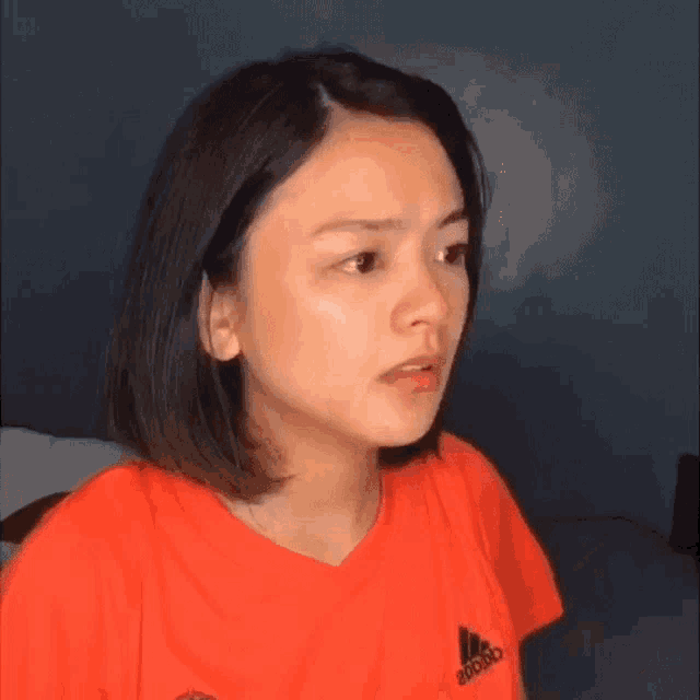 a woman wearing an orange adidas shirt is making a face .