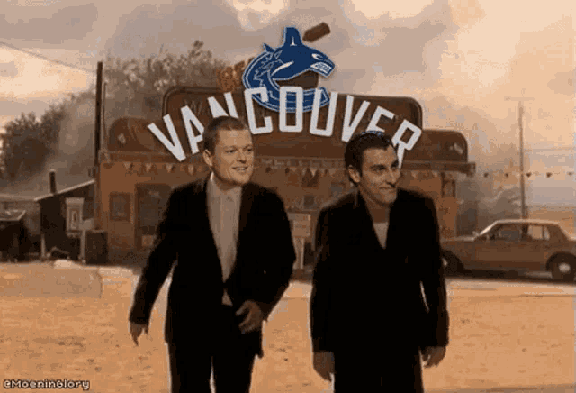 two men are walking in front of a sign that says vancouver