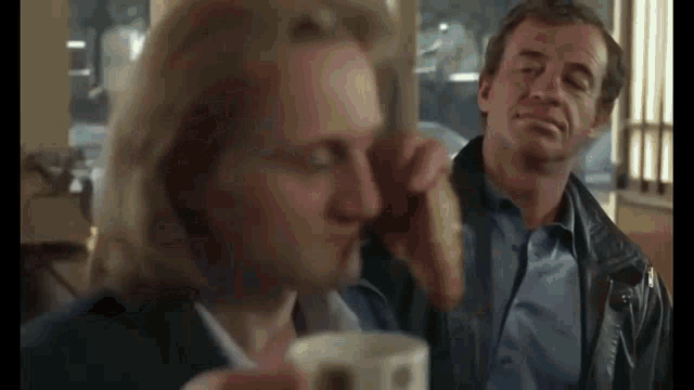 two men are sitting at a table with a woman holding a cup of coffee
