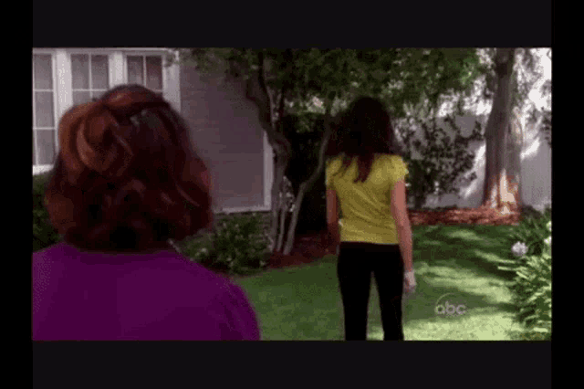 a woman in a yellow shirt stands in front of a house