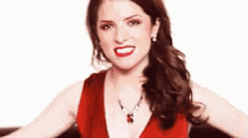 a woman in a red dress and necklace is smiling and making a funny face .