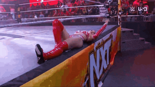a woman in red boots is laying on the edge of a wrestling ring next to an nxt banner