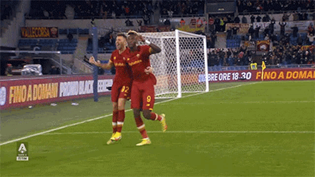 two soccer players celebrate a goal on a field with a sign that says fino a domani
