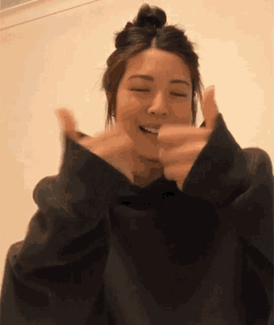 a woman in a black sweatshirt is giving a thumbs up sign .