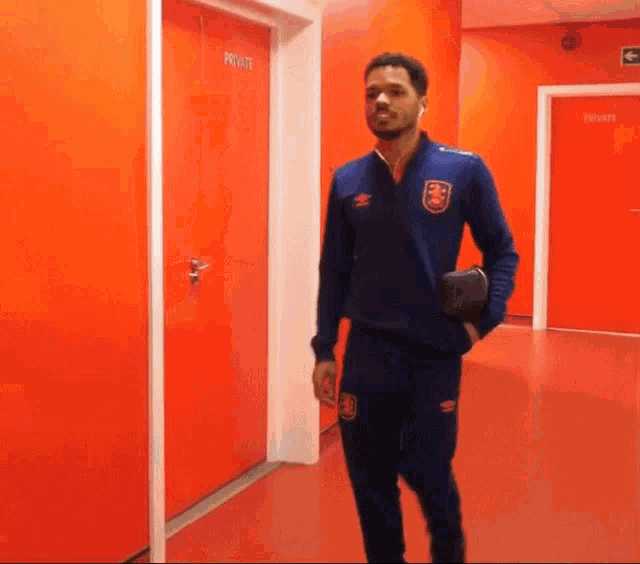 a man in a blue jacket stands in a hallway with red doors that say private