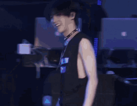 a man wearing a choker and a black tank top stands in front of an apple laptop