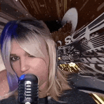 a woman with blue hair is singing into a microphone with a sign behind her that says s.c.