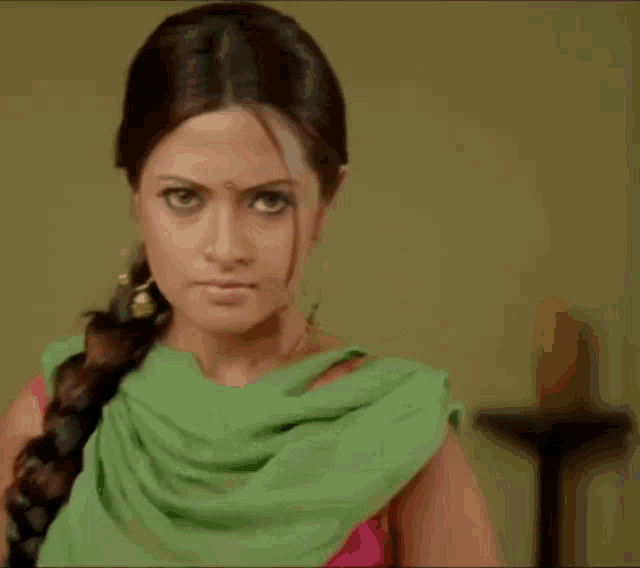 a woman wearing a green shawl and a pink top looks at the camera