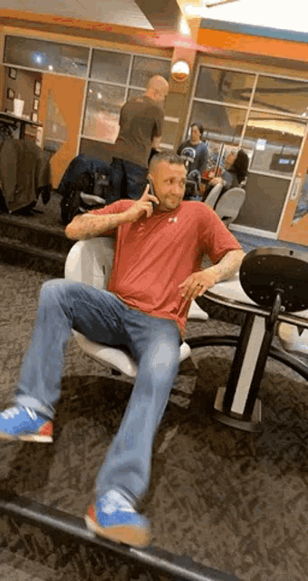 a man in a red shirt is sitting in a bowling alley giving a thumbs up