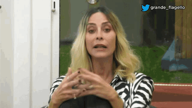 a woman in a zebra print shirt is sitting in front of a window with a twitter logo above her