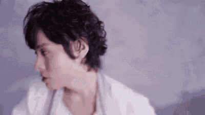 a man with curly hair is wearing a white shirt and a gray sweater .