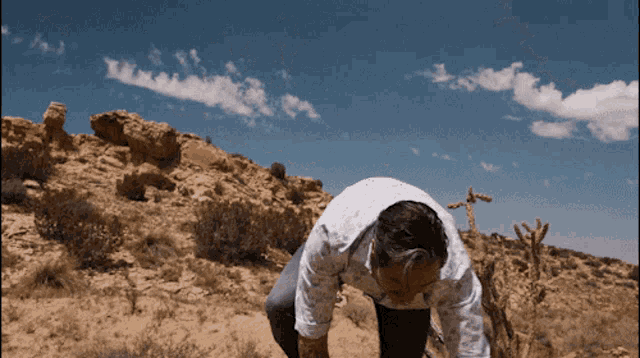 a man kneeling down in the desert with a blue sky in the background