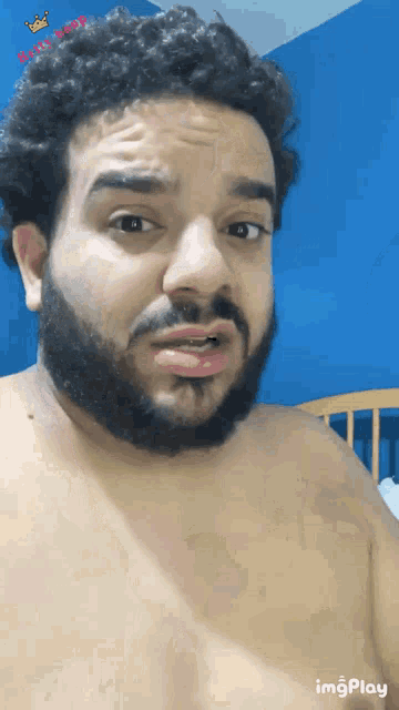 a shirtless man with a beard is making a funny face in front of a blue wall with the word king on it