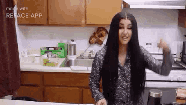 a woman with long black hair is standing in a kitchen with her hands in the air .