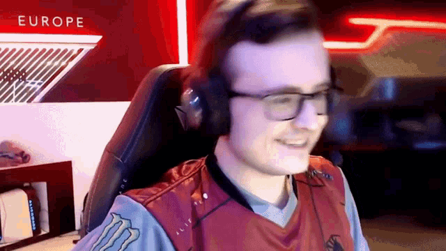 a man wearing headphones and glasses is sitting in a chair with the word europe on the wall behind him