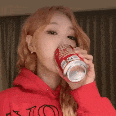 a woman in a red hoodie is drinking from a red can .