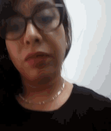 a woman wearing glasses and a necklace is making a funny face