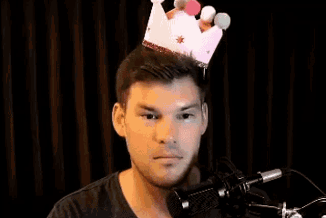 a man is wearing a pink crown on his head while standing in front of a microphone .