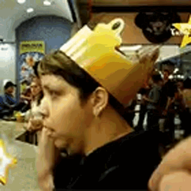 a man wearing a crown is sitting at a table in a crowded restaurant .