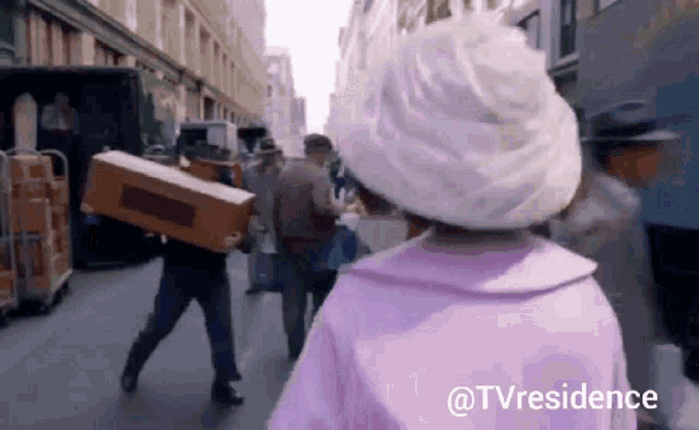 a woman in a white hat is walking down a street carrying boxes .