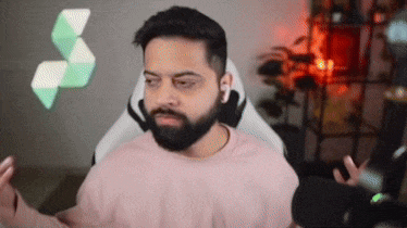 a man with a beard is wearing headphones and a pink sweater while sitting in a chair .