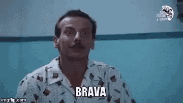 a man with a mustache is pointing at the camera while wearing a shirt that says brava .