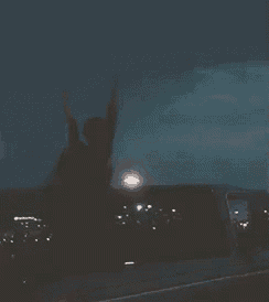 a person is standing in the back of a truck at night with their arms in the air .