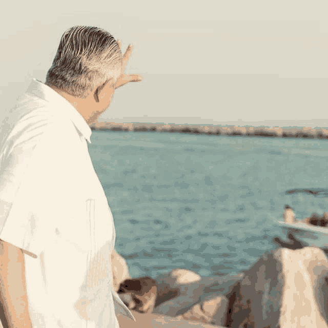 a man in a white shirt stands on a rock near the ocean