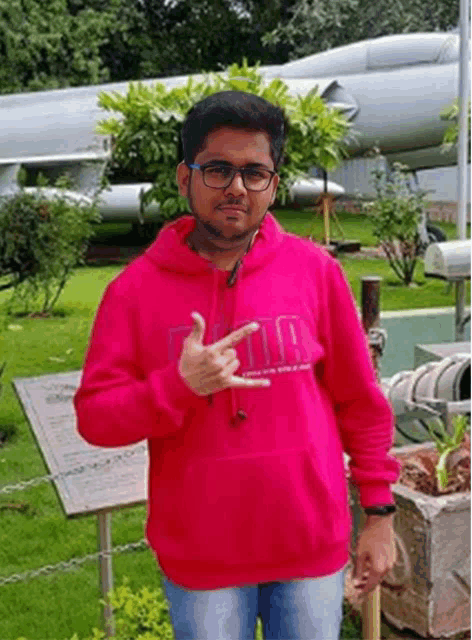 a young man wearing a pink hoodie is standing in front of a plane .