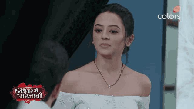 a woman wearing a white off the shoulder top and a black necklace is on a colors tv screen