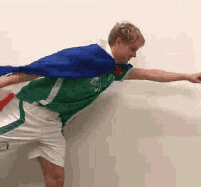 a man in a green shirt and white shorts is holding a blue cape over his shoulder .