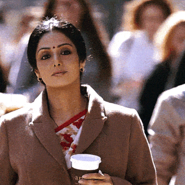 a woman in a tan coat holds a cup that says ' aar ' on it