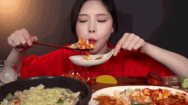 a woman in a red shirt is eating food with chopsticks and a spoon