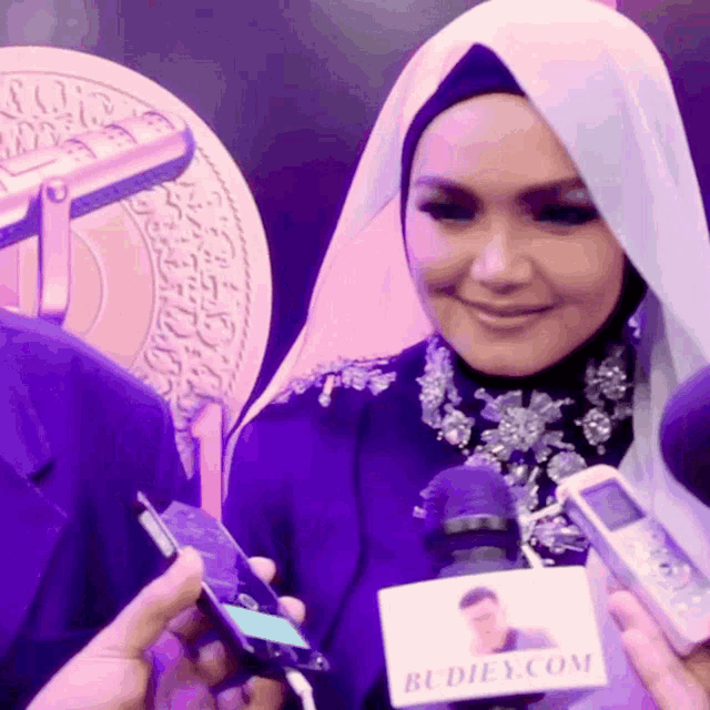 a woman wearing a hijab is being interviewed by a person holding a microphone that says budiey.com