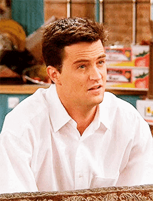 a man in a white shirt is sitting on a couch looking at something