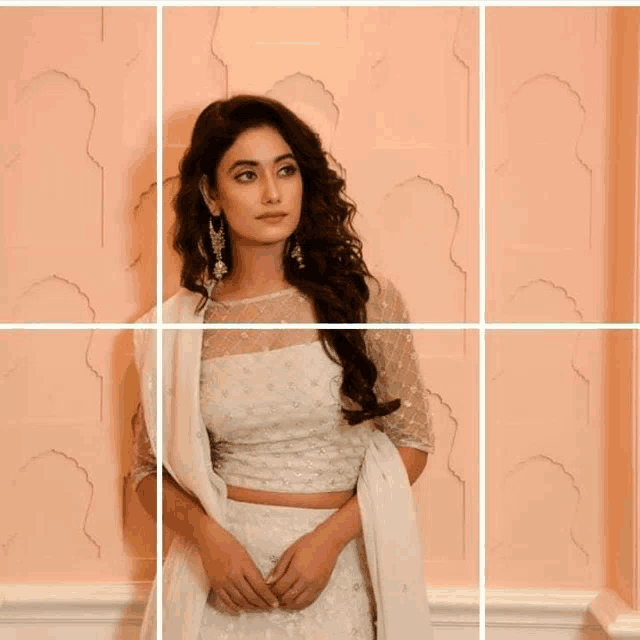 a woman in a white dress is standing in front of a wall