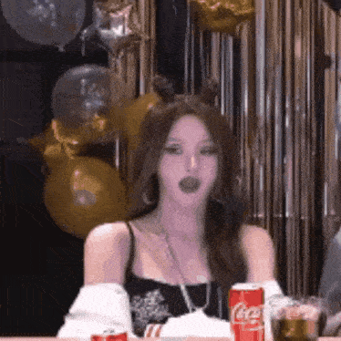 a woman is sitting at a table with a can of coca cola and balloons .