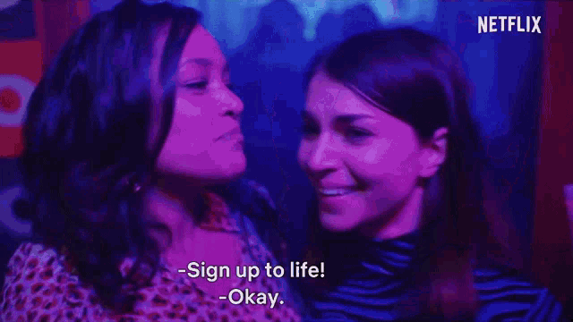 two women are standing next to each other in a club and one of them is saying " sign up to life okay " .