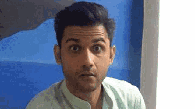 a man with a surprised look on his face is standing in front of a blue wall .