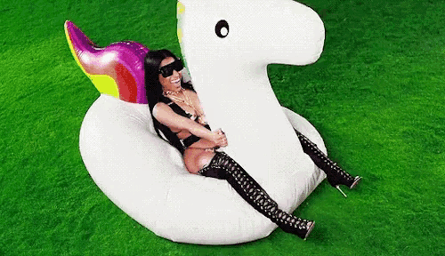 a woman is sitting on an inflatable unicorn on a green field .