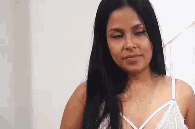 a woman with long black hair and a white bra is standing in front of a white wall .