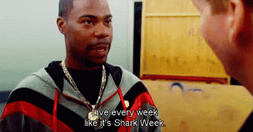 a man in a striped jacket is talking to another man and says live every week like it 's shark week .