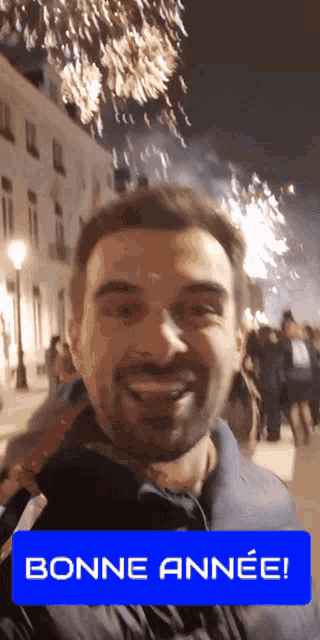 a man is smiling in front of a fireworks display with a bonne annee sign in the foreground